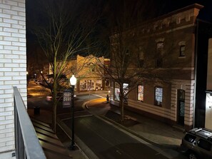 A nighttime street view with a building featuring a brick facade and illuminated windows.