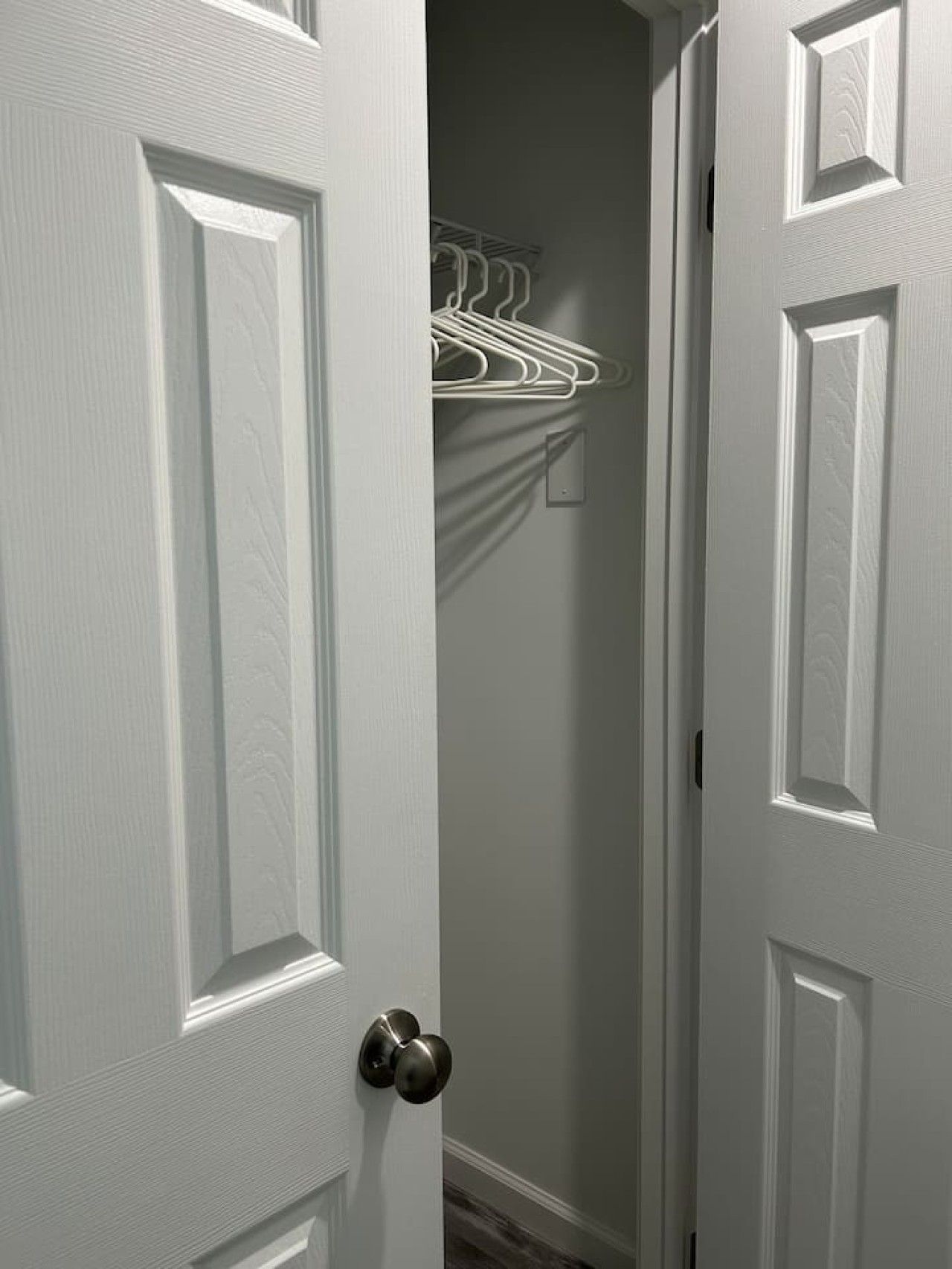 A white door with a modern handle, leading to a hallway with a white wall and a metal rack with clothes.