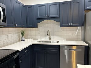 A modern kitchen with dark blue cabinets, a stainless steel dishwasher, and a white tiled backsplash. - Perfect Location Old town / walk to the VRE & BARS (Manassas)