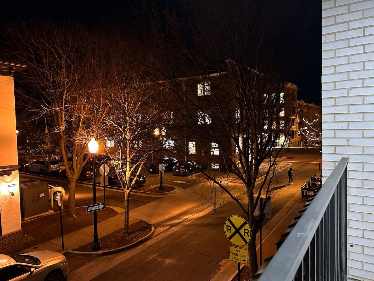 A nighttime street view with a railroad crossing sign, a one-way sign, and a building with illuminated windows.