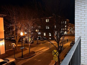 Vista nocturna de una calle con un cartel de paso a nivel y una señal de circulación en un solo sentido, y un edificio con ventanas iluminadas.