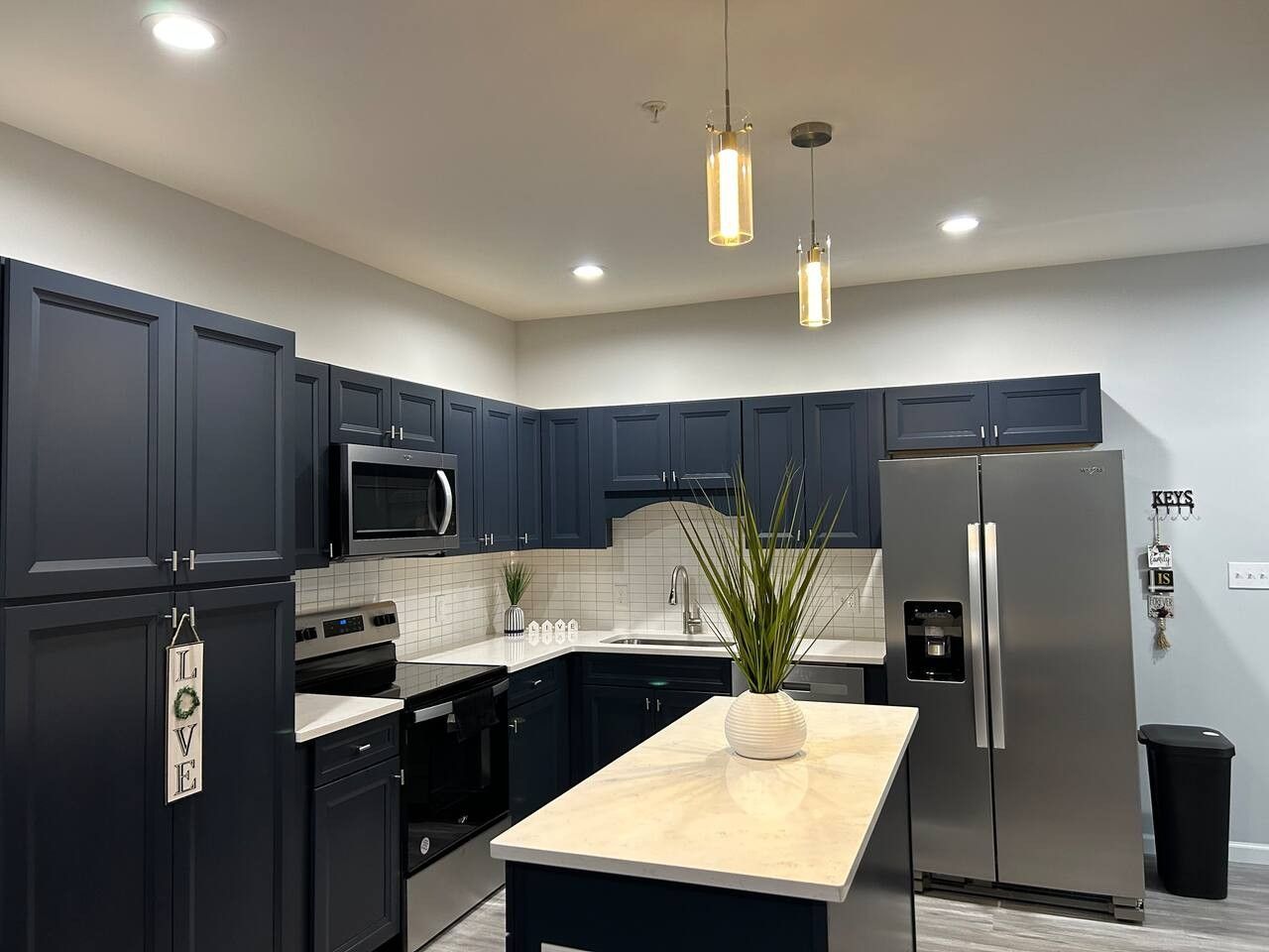A modern kitchen with dark cabinetry, stainless steel appliances, and pendant lighting.