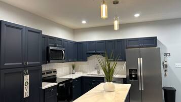 A modern kitchen with dark cabinetry, stainless steel appliances, and pendant lighting.