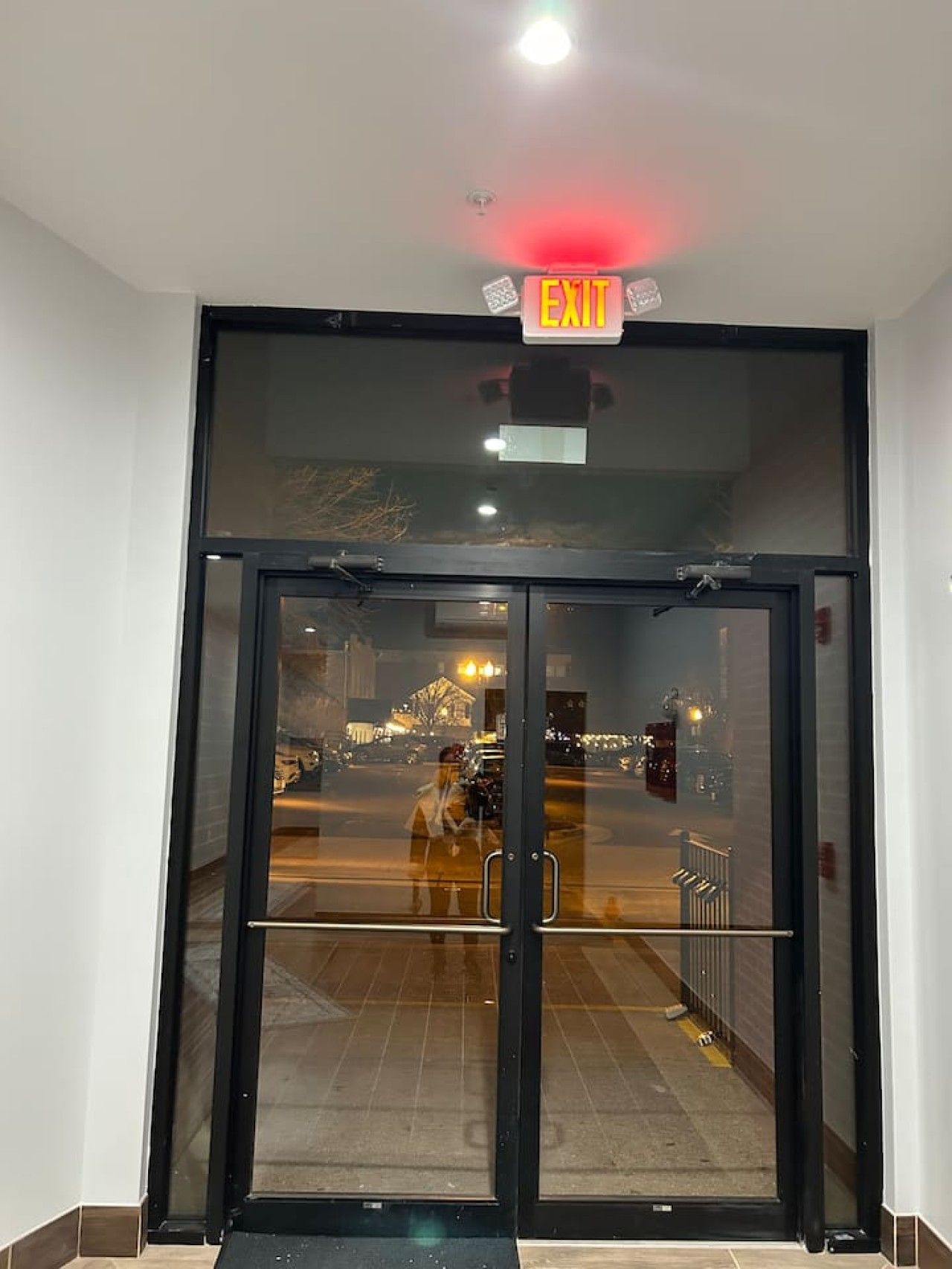 A hotel entrance with a glass door, an exit sign, and a view of the street outside.