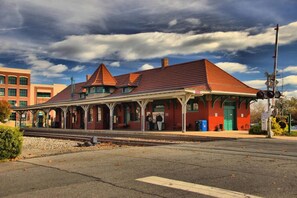 A historic train station with a covered platform, a clock tower, and a red building with green accents.