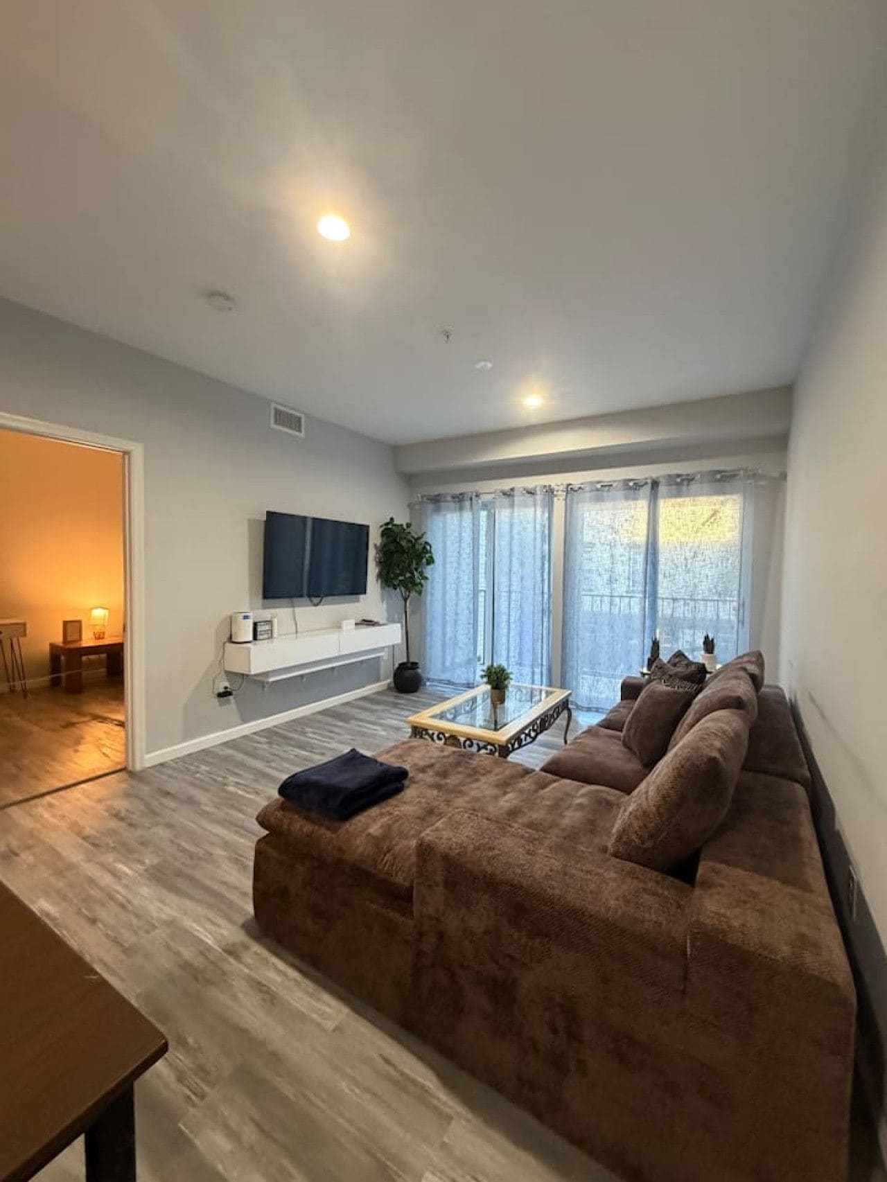 A modern living room with a brown sofa, a glass coffee table, and a TV mounted on the wall.