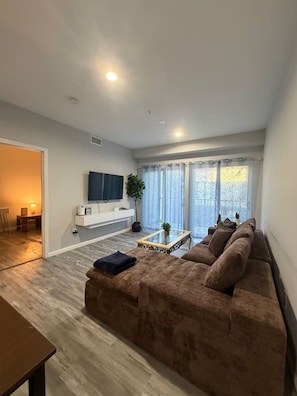 A modern living room with a brown sofa, a glass coffee table, and a TV mounted on the wall.