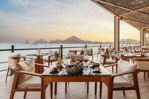 Restaurante com área externa e mesas de frente para um lago e paisagem montanhosa.