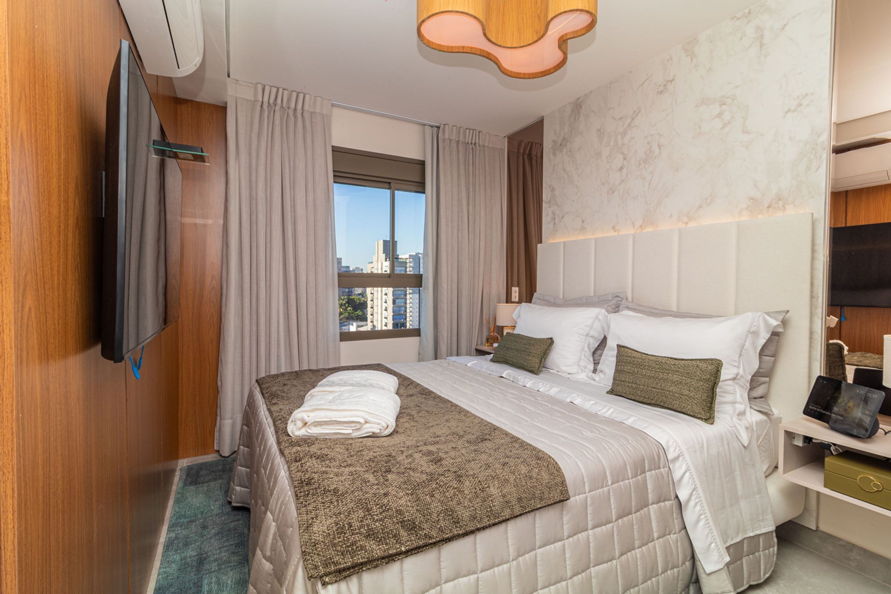 A hotel room with a bed, a TV, a window with curtains, and a city view.