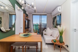 Uma sala de estar moderna com uma mesa de jantar, sofá e vista da cidade por grandes janelas.