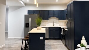 A modern kitchen with dark cabinets, a central island, and a dining area with a table and chairs. - Old Town Manassas Sleeps 4 next to bars and restaurants ,  WALK TO VRE (Manassas)