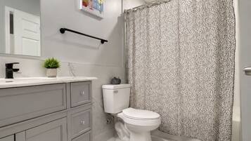A bathroom with a toilet, a shower curtain, a sink, and a mirror.