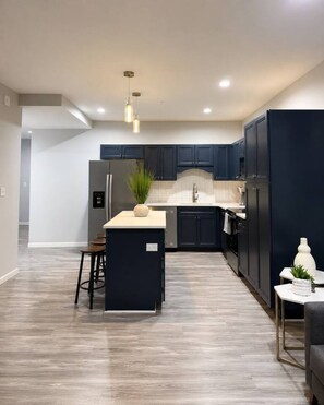 A modern kitchen with dark cabinets, a central island, and a dining area with a small table and chairs.