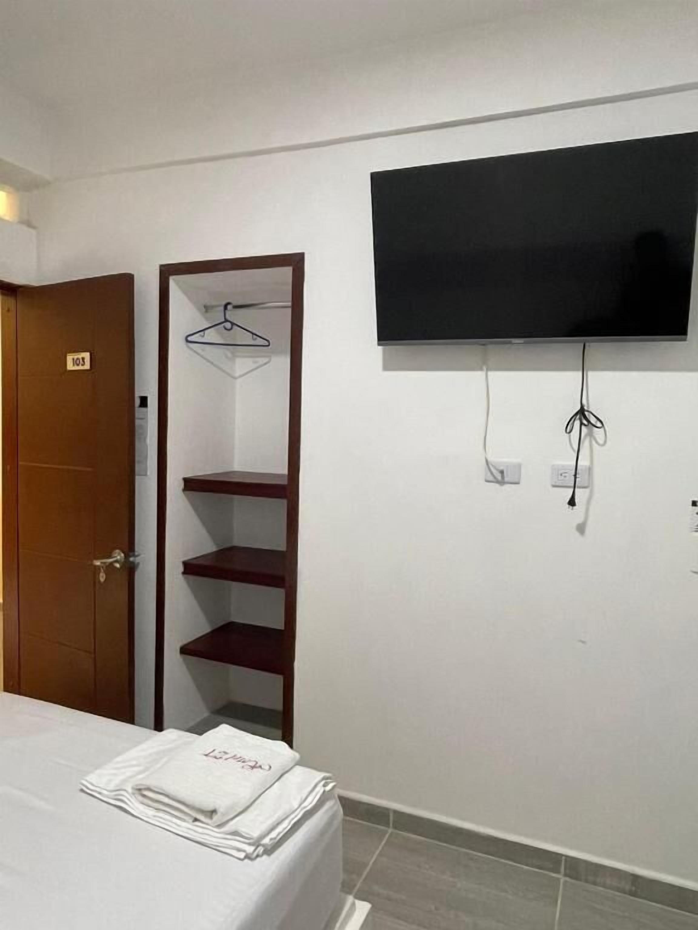 A hotel room with a bed, a TV mounted on the wall, a wooden wardrobe, and a door labeled '105'.