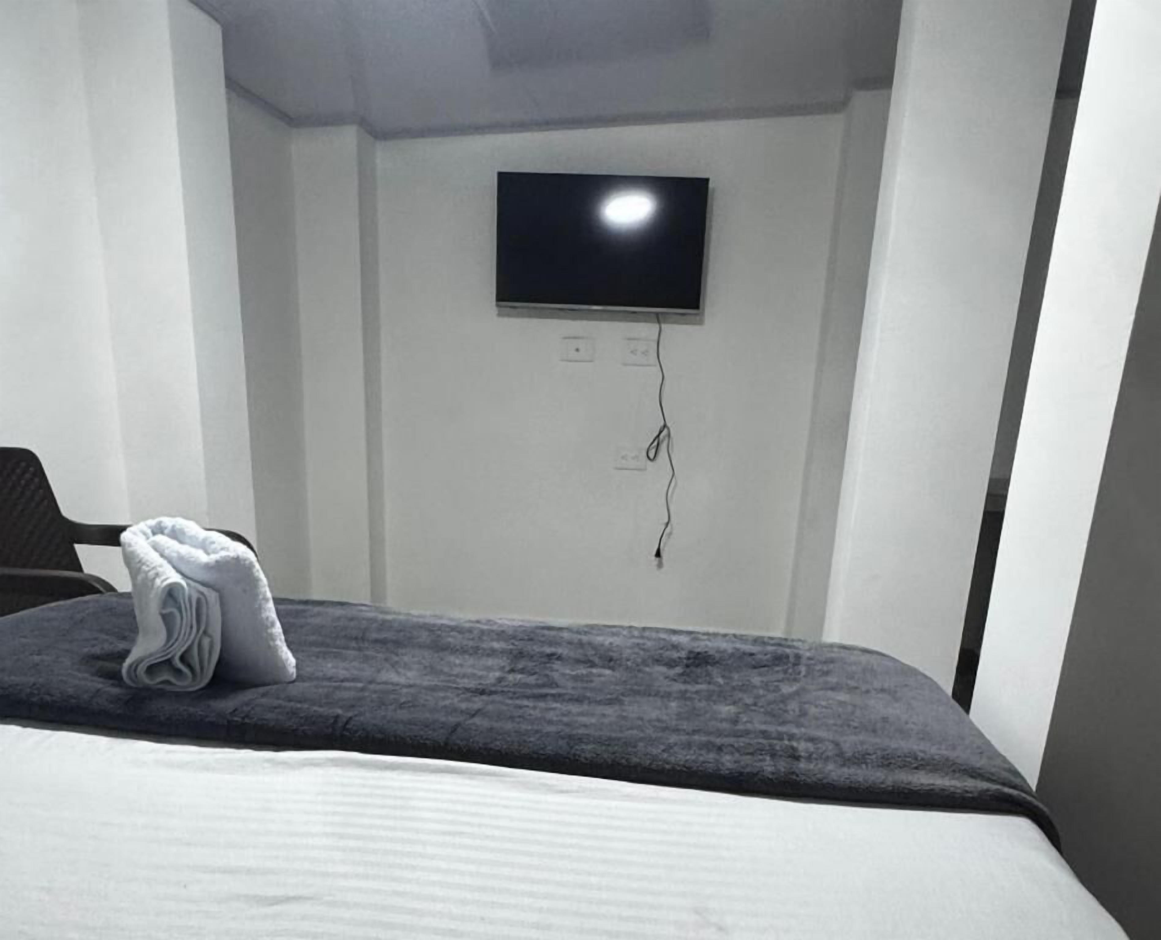 Habitación de hotel con cama, televisor de pantalla plana montado en la pared y una toalla doblada sobre la cama.