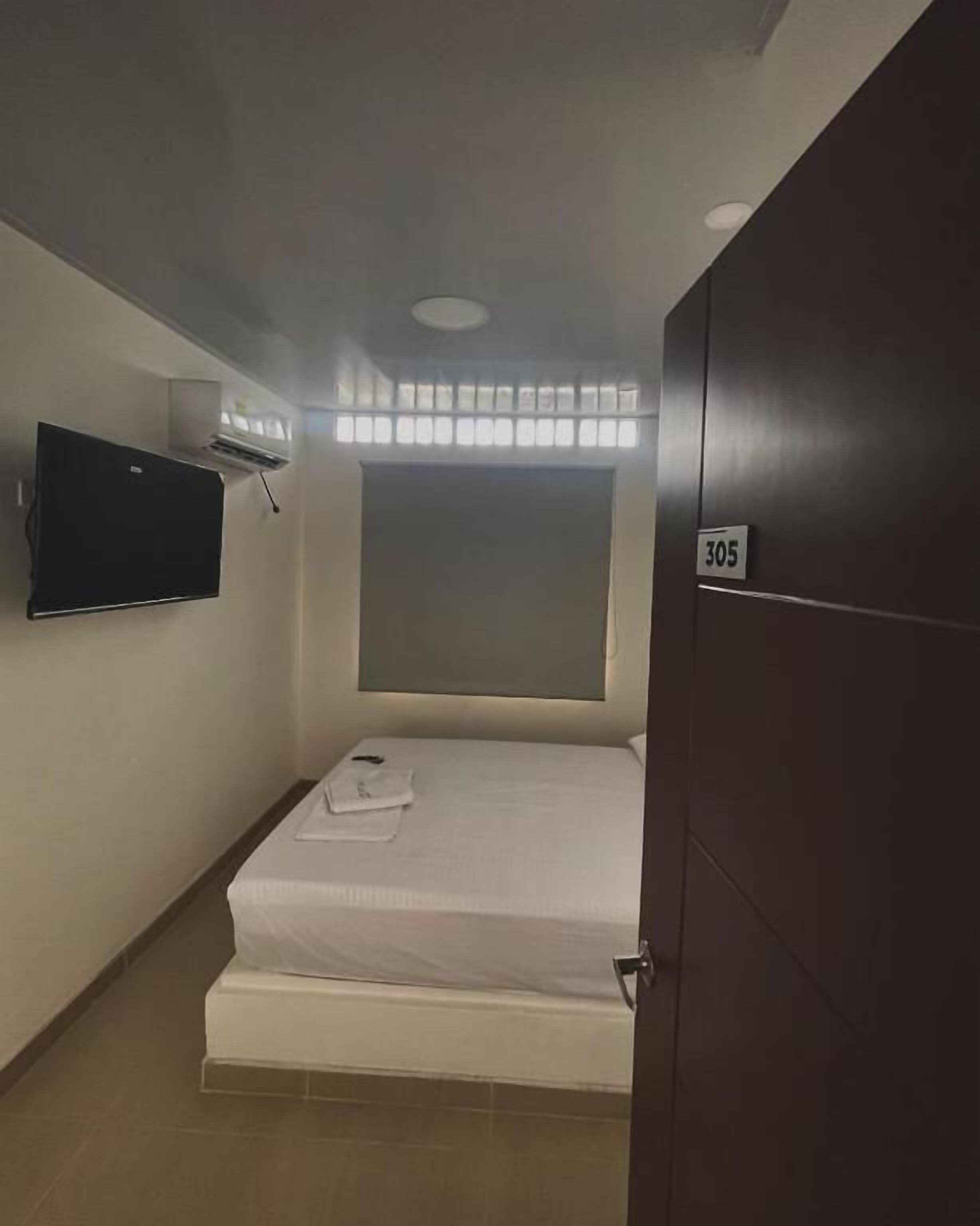 A hotel room with a bed, a television mounted on the wall, and a door with a number.