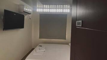 A hotel room with a bed, a television mounted on the wall, and a door with a number.