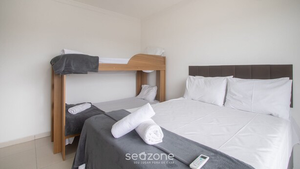 A hotel room with a bunk bed, a single bed, and a remote control on the bed. - House w/ 2 Suites in a Cond. w/ Pool Blv0004 (Porto Seguro)
