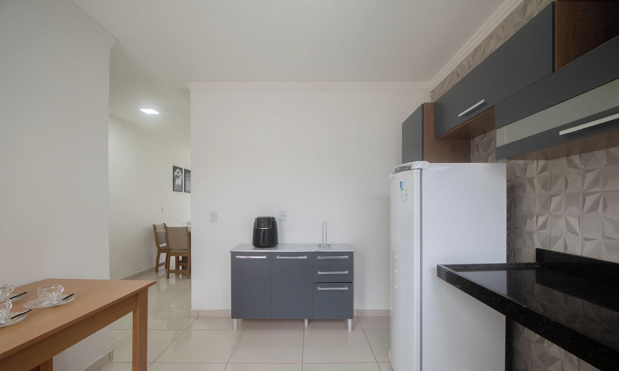 Uma cozinha compacta com geladeira, cafeteira e área de refeições com cadeiras e mesa.