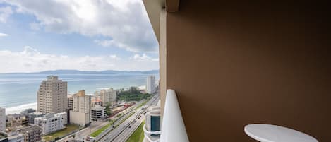 A balcony with a view of the sea, a road, and surrounding buildings.