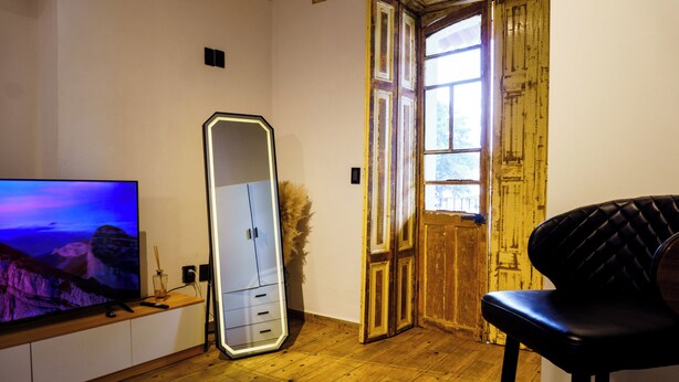 Ein Zimmer mit Holzboden, einem Fernseher auf einem Schrank, einem Spiegel und einer Tür mit Fenster.