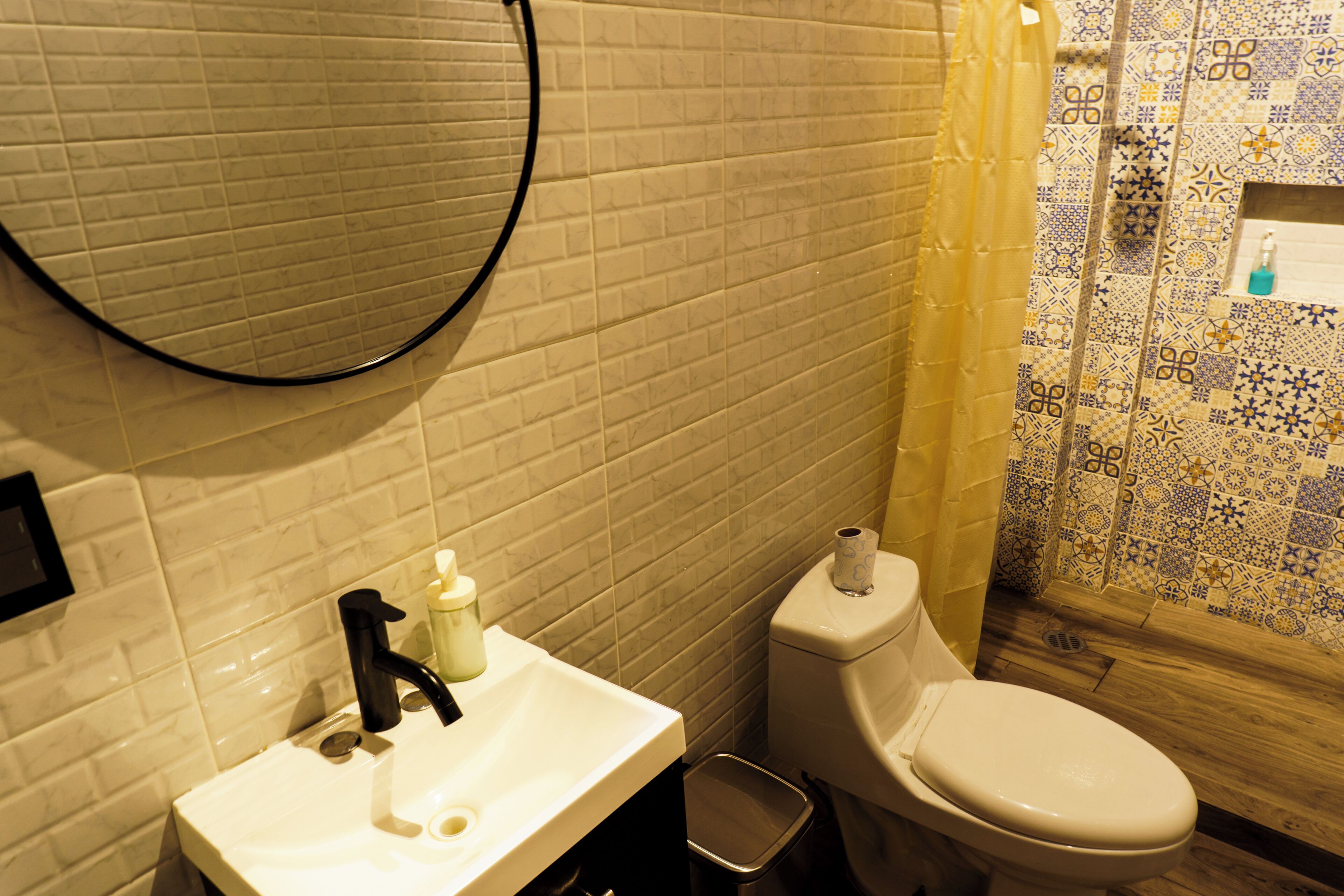Une salle de bain avec un lavabo blanc, un robinet noir et des toilettes avec un rouleau de papier toilette.