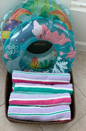 Una cesta con una almohada de colores con temática playera y toallas a rayas.