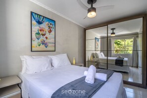Quarto de hotel com uma cama grande, um ventilador de teto, um quadro e vista por uma porta de vidro.