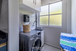 Uma lavanderia compacta com máquina de lavar, varal, pia e janela com vista.