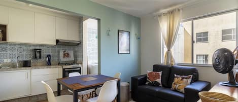 A compact living space with a kitchenette, dining area, and a sofa with a view of the city.