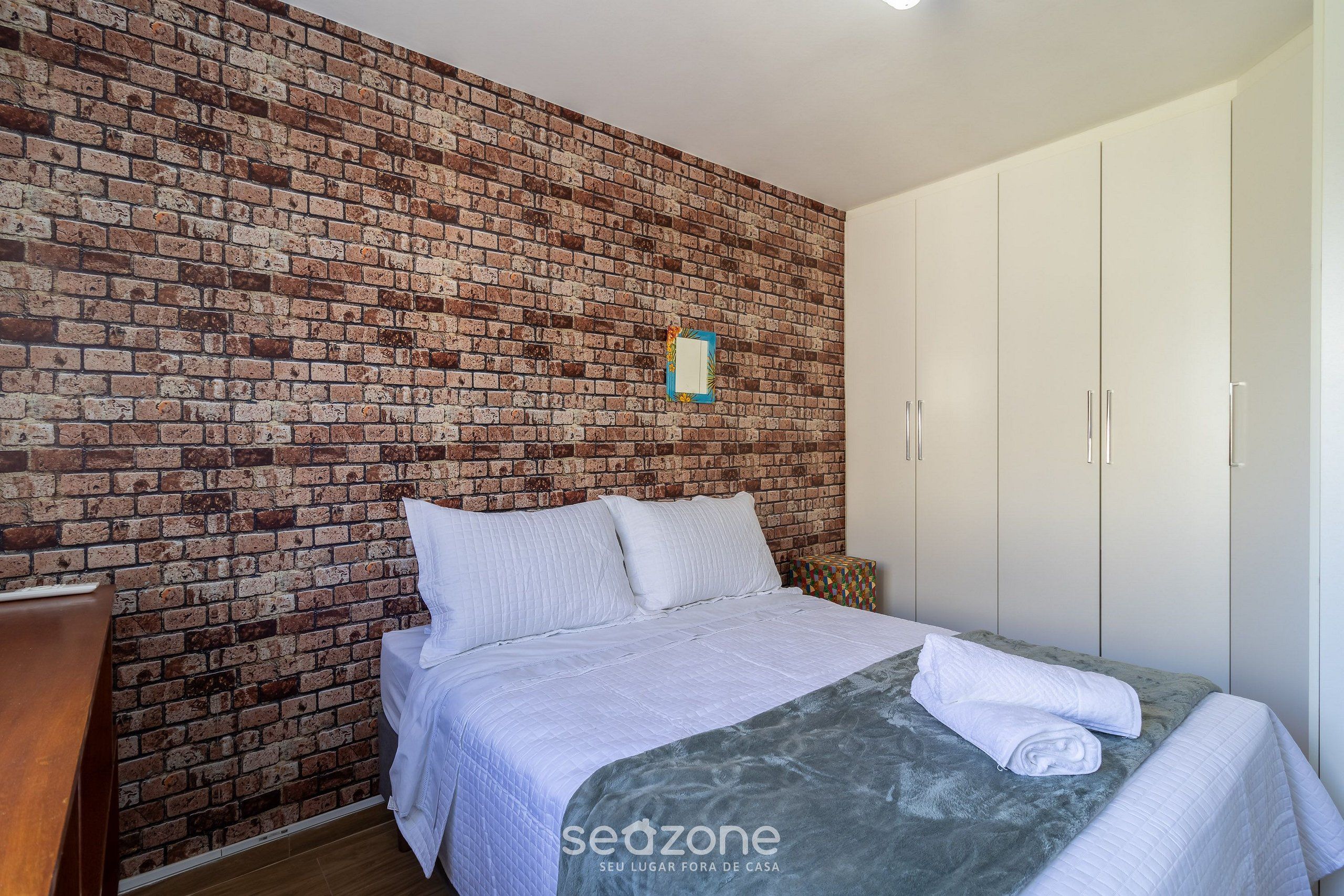 A bedroom with a brick wall, a bed with white bedding, and a wardrobe.