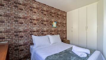 A bedroom with a brick wall, a bed with white bedding, and a wardrobe.