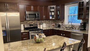 A kitchen with dark wood cabinets, stainless steel appliances, a granite countertop, and three bar stools.