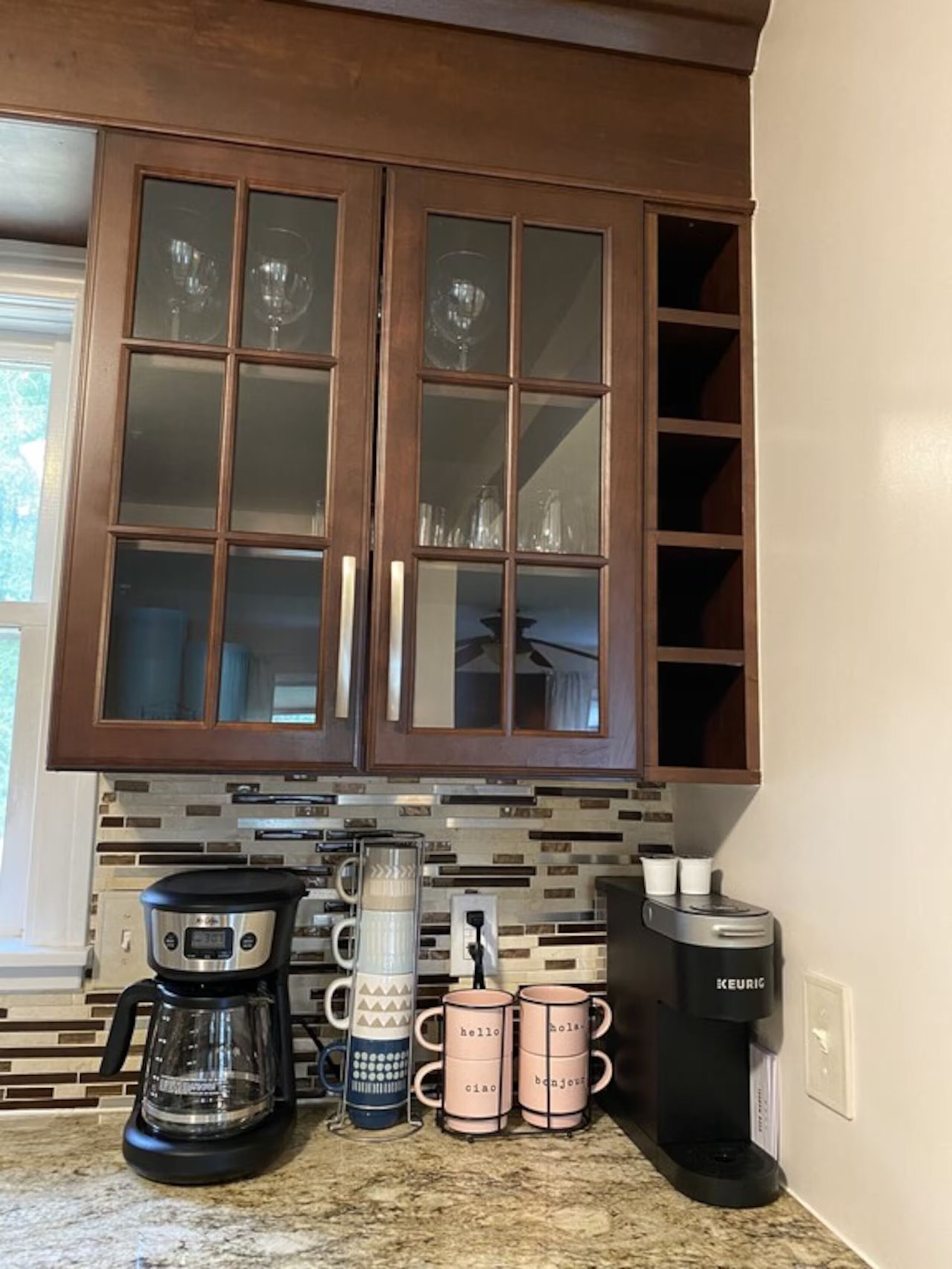 A kitchen with wooden cabinets, a coffee maker, and three mugs with text.