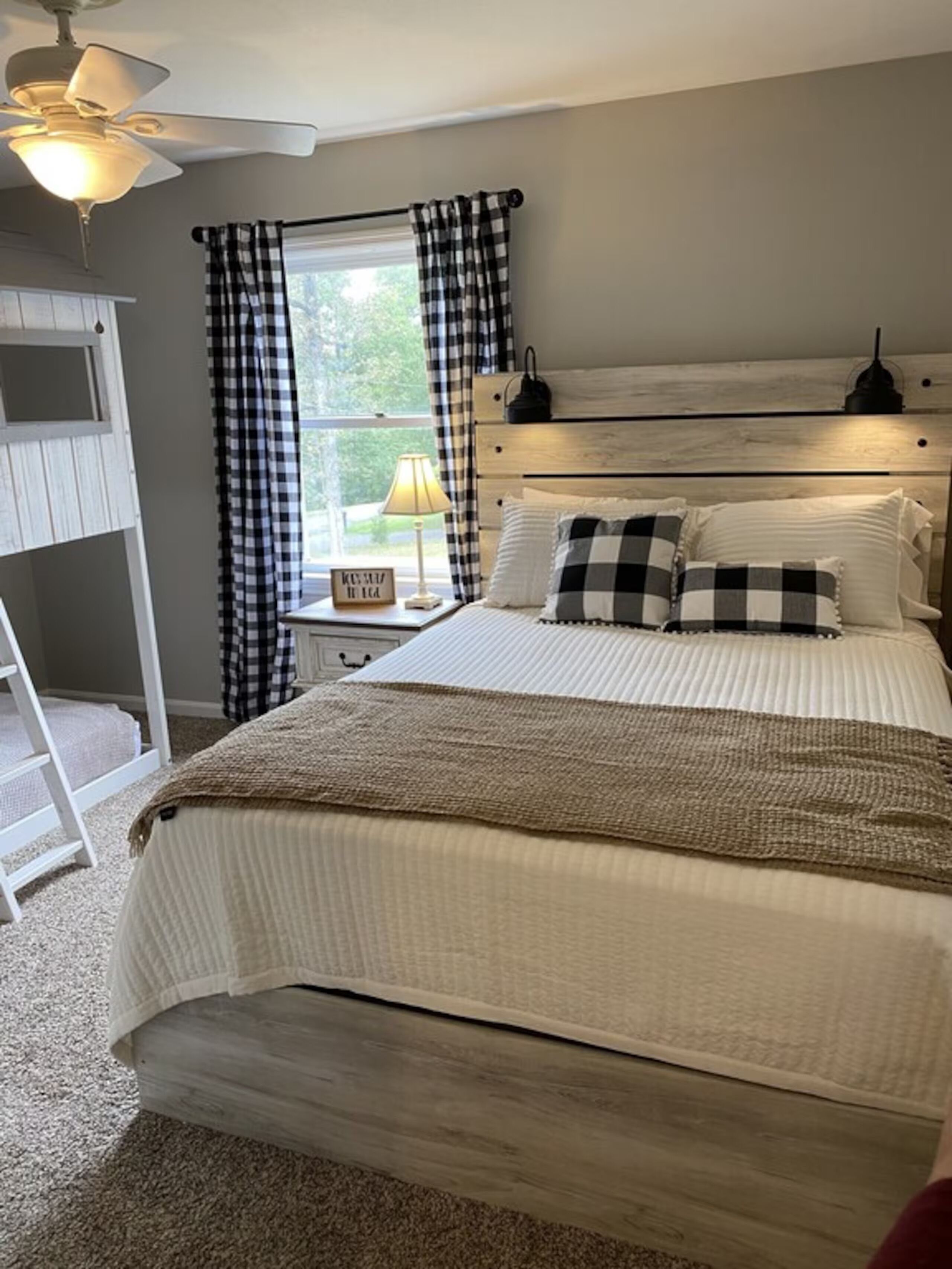 A bedroom with a bed, a nightstand, a lamp, a window with curtains, and a ceiling fan.