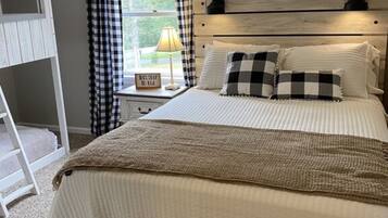 A bedroom with a bed, a nightstand, a lamp, a window with curtains, and a ceiling fan.