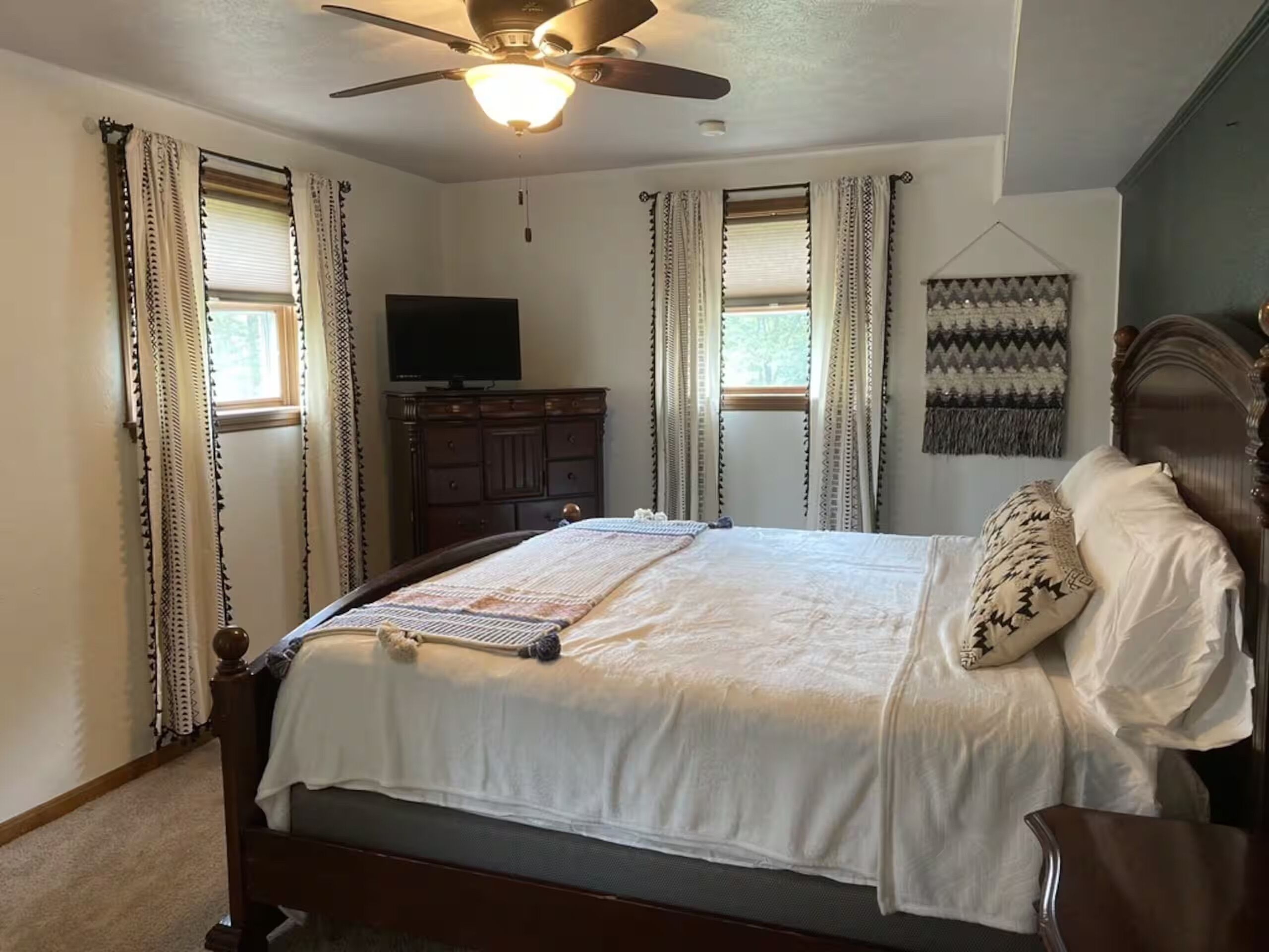 Une chambre à coucher comprenant un lit, un ventilateur de plafond, un téléviseur, une commode et un tableau ou une décoration murale.