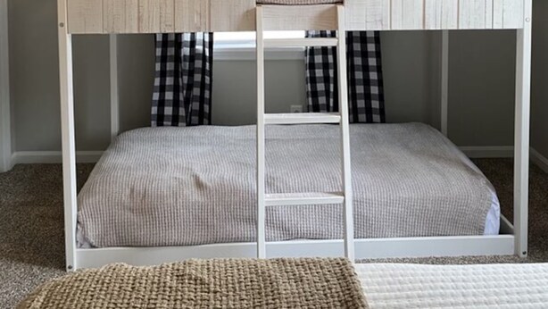 A bunk bed with a ceiling fan, a window with curtains, and a small mirror.
