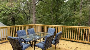 A deck with a glass-top table and six chairs with patterned cushions.