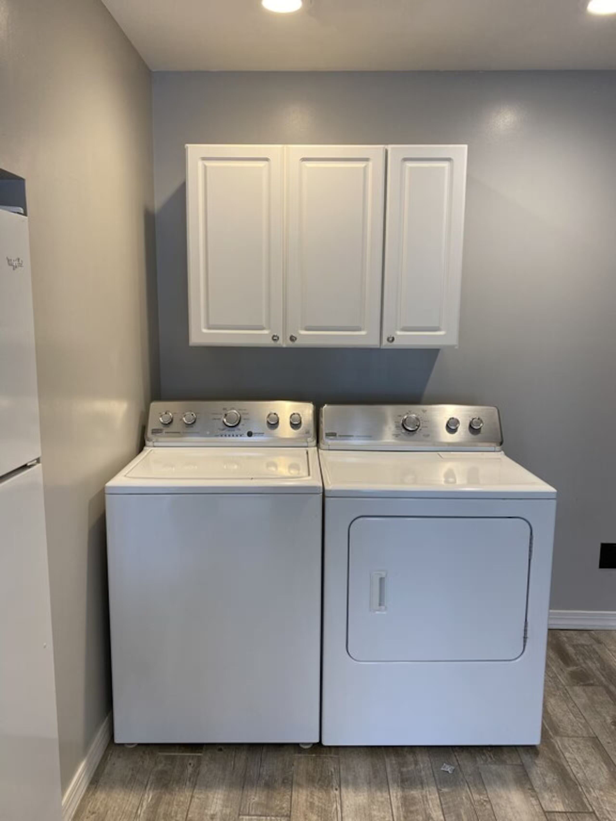 A laundry area with a washer and dryer, a white refrigerator, and a set of cabinets above the appliances.