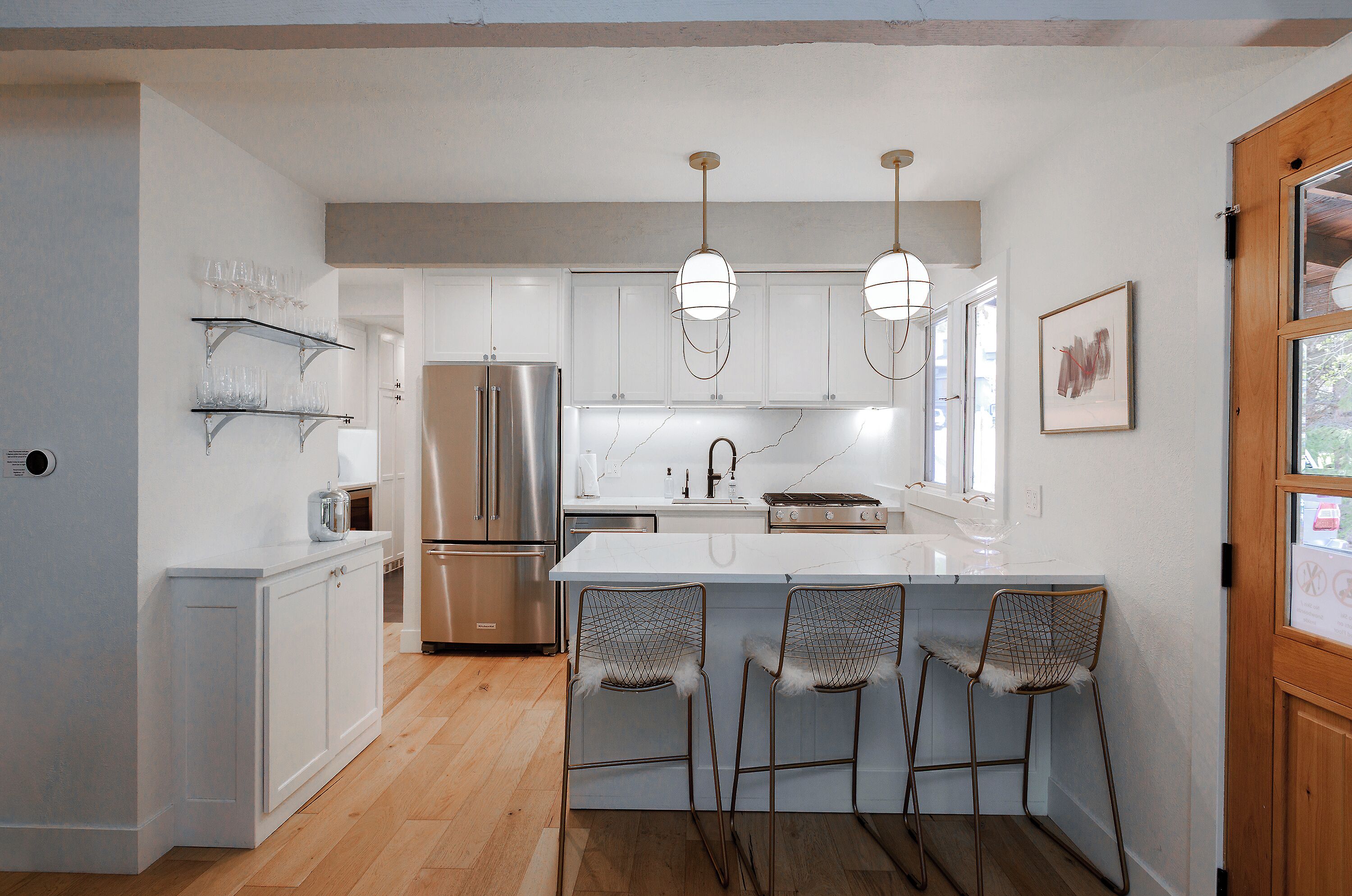 Una cocina moderna con muebles blancos, electrodomésticos de acero inoxidable y una zona de bar con sillas metálicas.