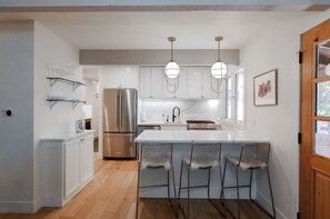 A modern kitchen with white cabinetry, stainless steel appliances, and a bar area with metal chairs. - 3BR West Vail duplex with river views, hot tub, fireplace, and deck. (Vail)