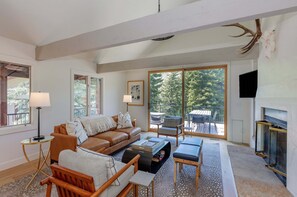 A spacious living room with a large window, a fireplace, and a ceiling with antlers. - 3BR West Vail duplex with river views, hot tub, fireplace, and deck. (Vail)