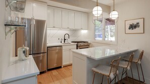 A modern kitchen with stainless steel appliances, a marble countertop, and a large island with bar stools. - 3BR West Vail duplex with river views, hot tub, fireplace, and deck. (Vail)