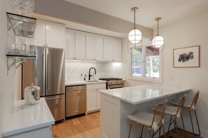A modern kitchen with stainless steel appliances, a marble countertop, and a large island with bar stools. - 3BR West Vail duplex with river views, hot tub, fireplace, and deck. (Vail)
