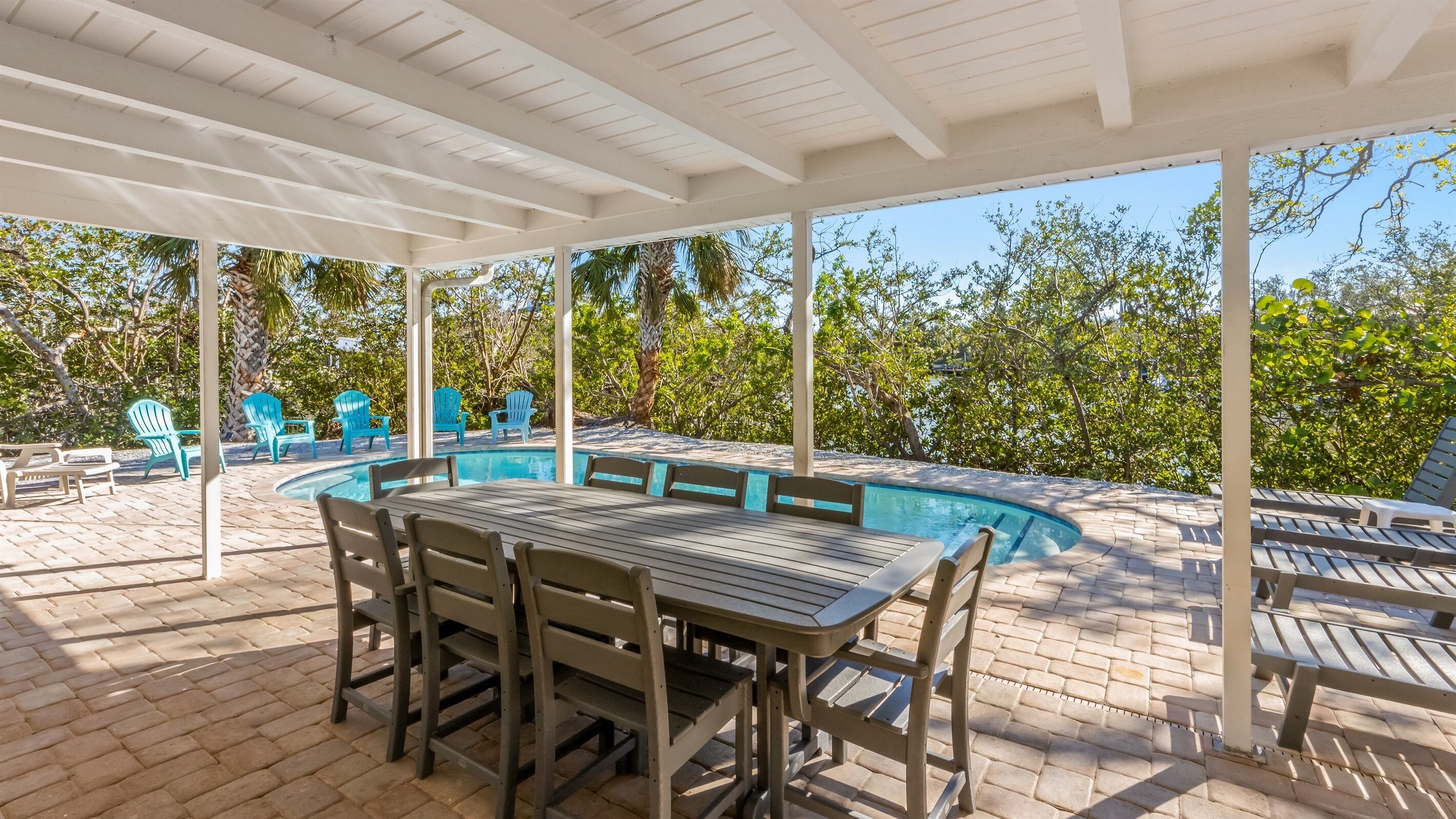 An outdoor pool area with a covered patio, lounge chairs, and a table.
