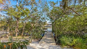 A pathway leading to a building surrounded by dense foliage and a wooden deck. - Beach meets Bay: Your Private Poolside Beach-Boat-Bay-Paradise (Anna Maria)