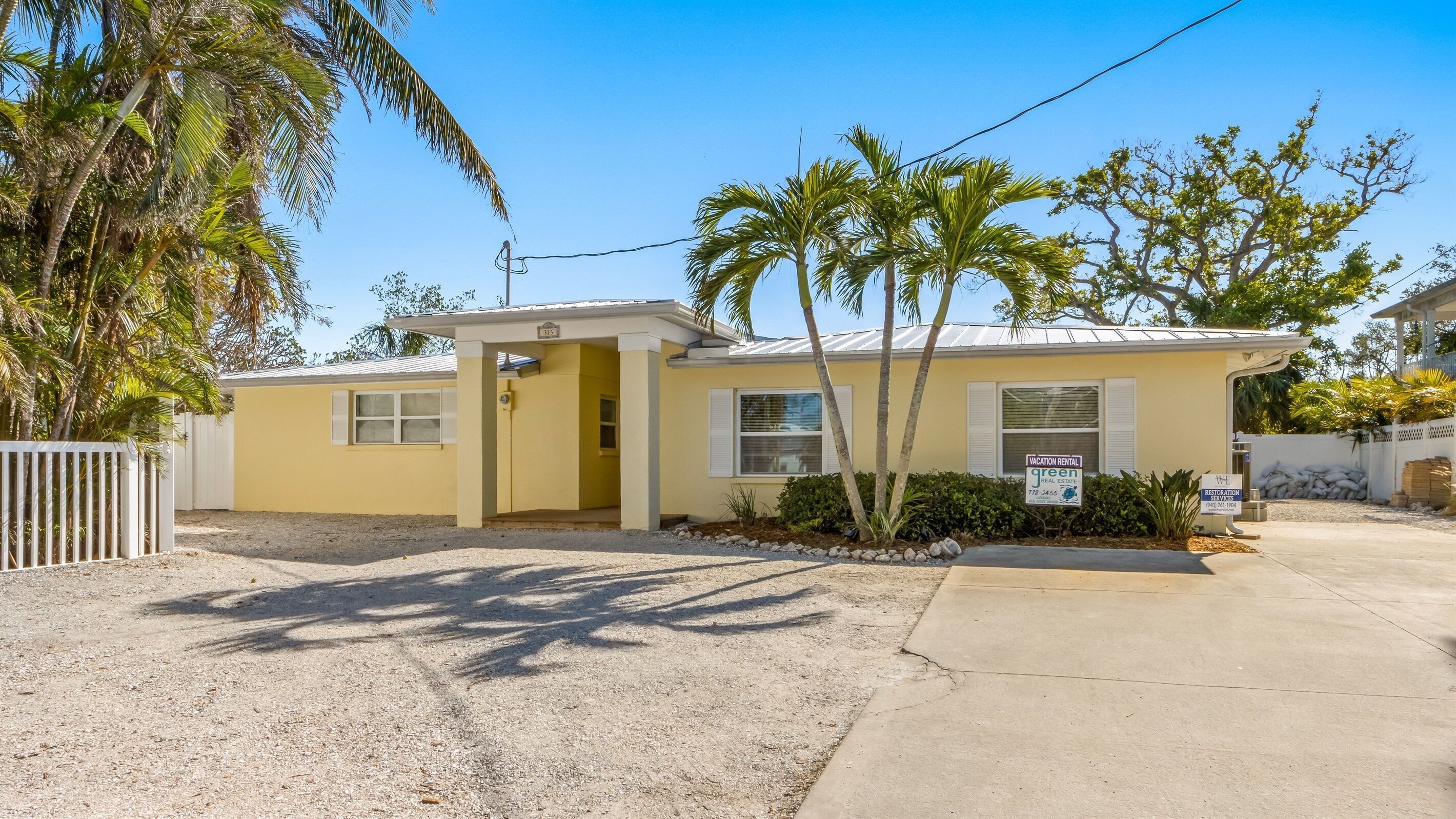 A single-story yellow building with a gated entrance, a small porch, and a sign indicating it's a vacation rental.