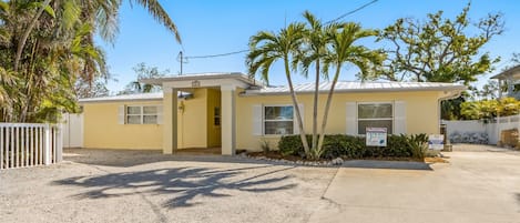 A single-story yellow building with a gated entrance, a small porch, and a sign indicating it's a vacation rental.