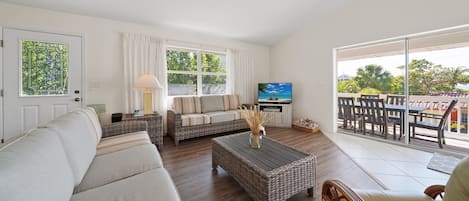 Ein Wohnzimmer mit einer Couch, einem Couchtisch, einem Fernseher und einem Balkon mit Gartenmöbeln.